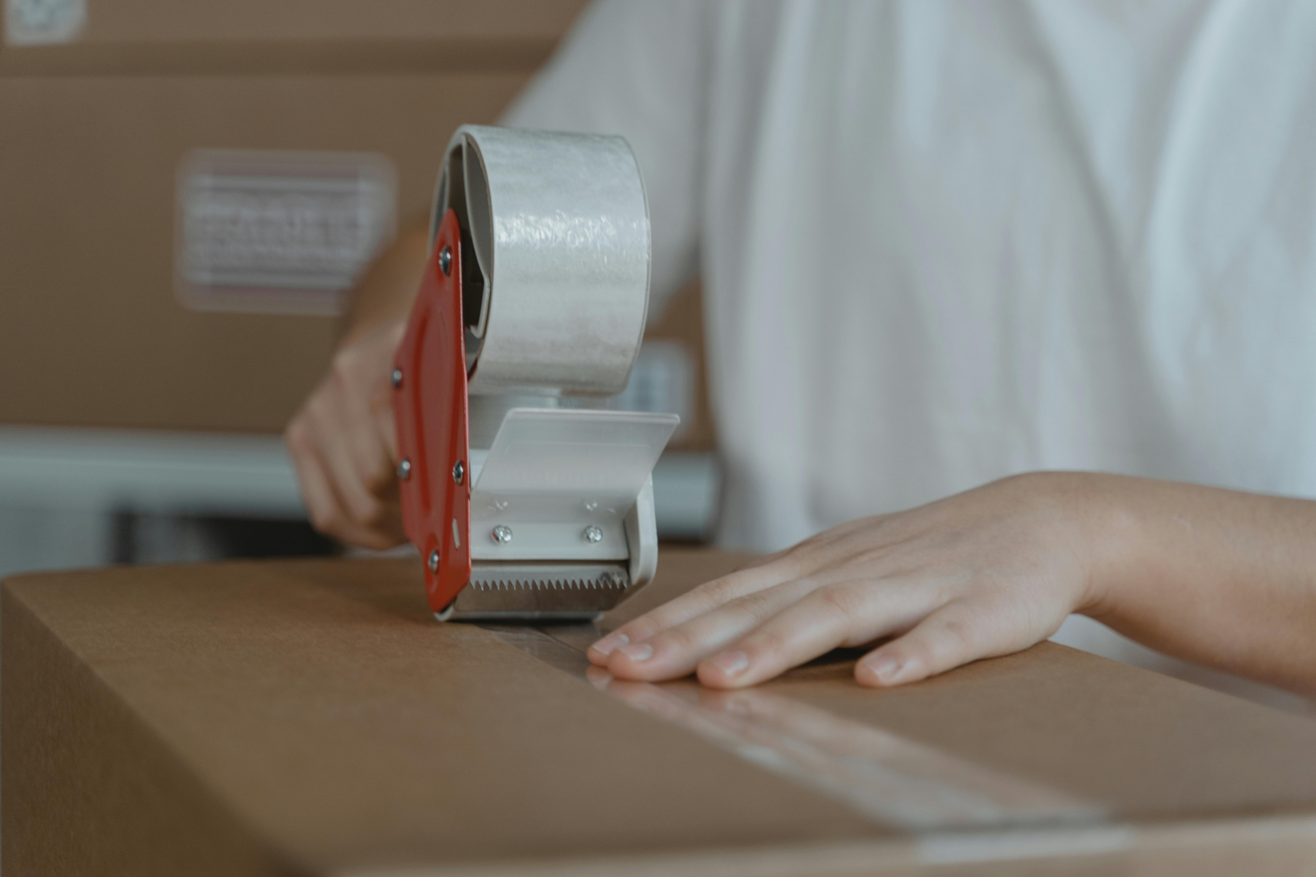 Person holding down a cardboard box while applying adhesive tape to the top of it