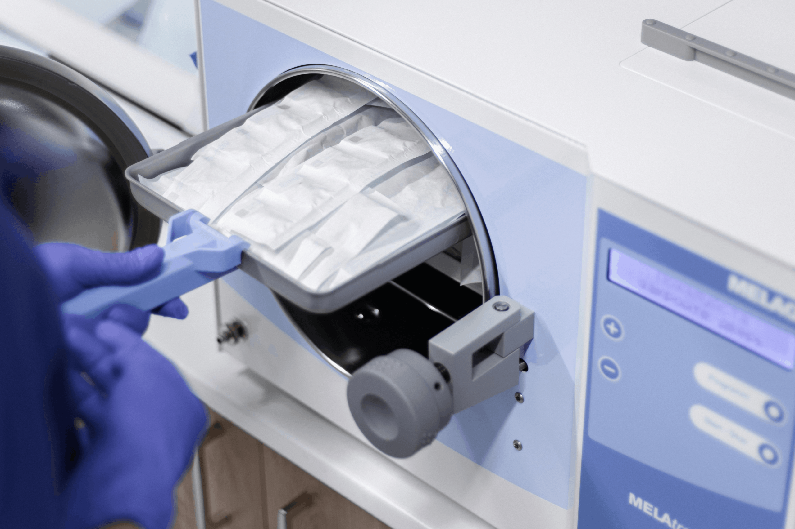 Gloved technician loading sterilized instruments into a machine.