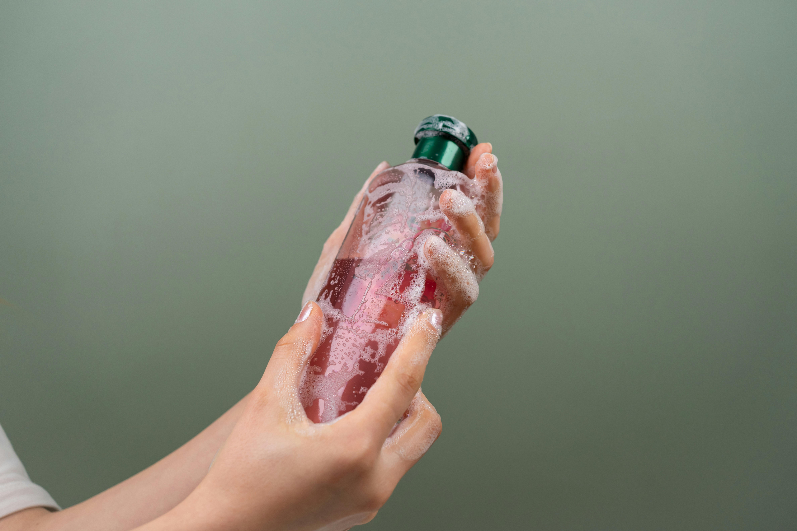 Hands holding a pink hair care bottle against a soft gray background